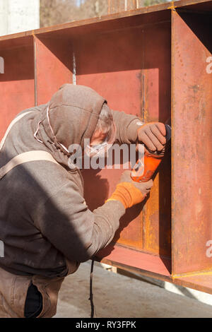 Ein Mitarbeiter in weißen Overalls und eine schützende Maske Prozesse mit elektrischen Flexion einer metallischen Struktur Stockfoto