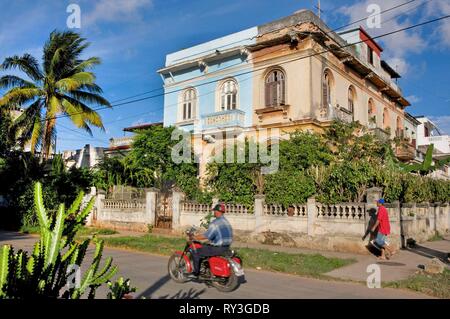 Kuba, la Haban, Vedado, Mann auf einem alten Motorrad vor einem barocken Villa in einem ruhigen und grünen Stadtteil fahren Stockfoto