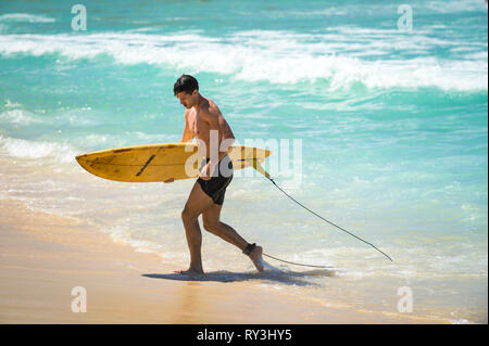 RIO DE JANEIRO - Februar 9, 2017: Eine junge Brasilianische surfer Spaziergänge mit seinem Surfbrett über die Wellen an Arpoador, der beliebten Surf Break auf Ipanema. Stockfoto