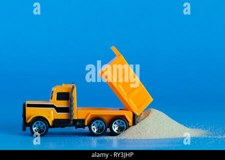 Gelb Spielzeug-LKW gießt Sand auf dem blauen Hintergrund. Konzept der Konstruktion. Stockfoto
