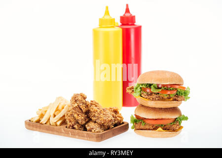 Knusprige Chicken Nuggets, Hamburger und Pommes frites in der Nähe von Flaschen mit Ketchup und Senf isoliert auf weißem Stockfoto