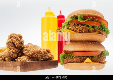 Selektiver Fokus der crispy Chicken Nuggets und Chicken Burger in der Nähe von Flaschen mit Ketchup und Senf isoliert auf weißem Stockfoto