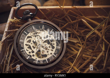 Pocket Watch Winder auf natürlichen Weizen Stroh in einer Holzkiste. Konzept der Vintage oder retro Geschenk. Stockfoto