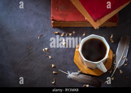 Schwarzen Kaffee in weißen Schale und alte Bücher mit Feder und getrockneten Blütenblätter auf dem marmortisch und Morgen sunlight. Stockfoto