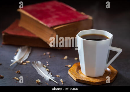 Schwarzen Kaffee in weißen Schale und alte Bücher mit Feder und getrockneten Blütenblätter auf dem marmortisch und Morgen sunlight. Stockfoto
