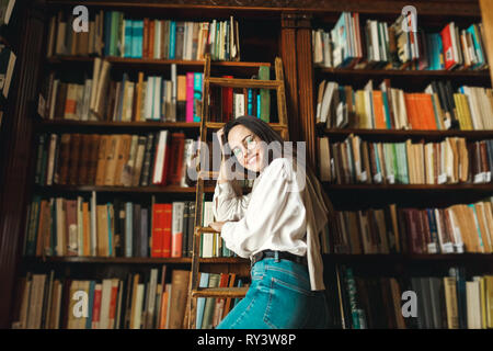 Stehendes Mädchen vor dem Hintergrund der Bücherregale in der Bibliothek Stockfoto