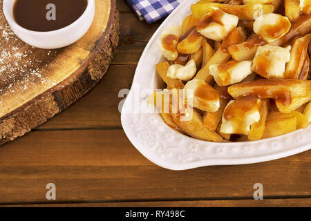 Poutine Platte auf einem hölzernen Hintergrund. Mit Pommes frites, Soße und Quark zubereitet. Kanadische Küche. Stockfoto