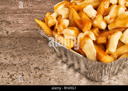 Teilweise hautnah auf einer Poutine in einem takeout Container. Mit Pommes frites, Rindfleisch, Soße und Quark Käse gekocht. Stockfoto