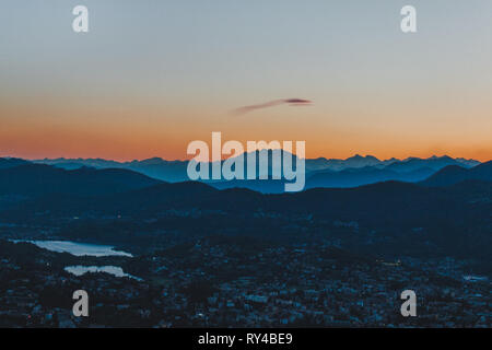 Eine faszinierende Cloud glühende über die Schichten der Schweizer und italienischen Alpen, mit der schönen Stadt Lugano im Vordergrund. Stockfoto