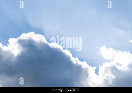 Die Strahlen der Sonne hinter den Wolken im blauen Himmel. Stockfoto