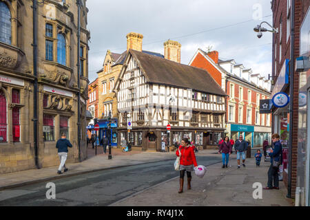 Menschen Shopper Shopping auf der High Street im Shropshire Markt Stadt Oswestry mit Blick auf die schwarz-weiße Fachwerkhaus Llwyd Mansion. Stockfoto