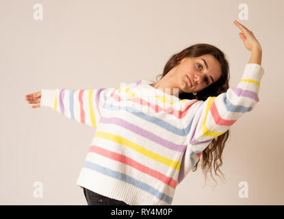 Portrait von Wunderschöne und glückliche Brünette blonde Mädchen in bunt gestreiften Pullover tanzen und stellt auf neutralem Hintergrund. In positive Emotionen, da Stockfoto