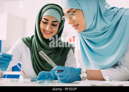 Lächelnd weibliche muslimische Wissenschaftler holding Pipette und Glas Reagenzglas im chemischen Labor experimentieren Stockfoto