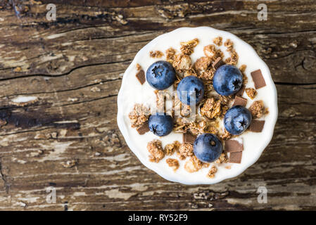 Servieren von Joghurt mit ganzen frischen Blaubeeren und Müsli auf alten rustikalen Holztisch. Closeup Detail. Stockfoto