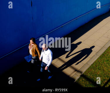 Ein paar Hand in Hand werfen ihre Schatten hinter Ihnen, da sie Unterführung im hellen Sonnenschein Ein, Fort William High Street lochaber Stockfoto