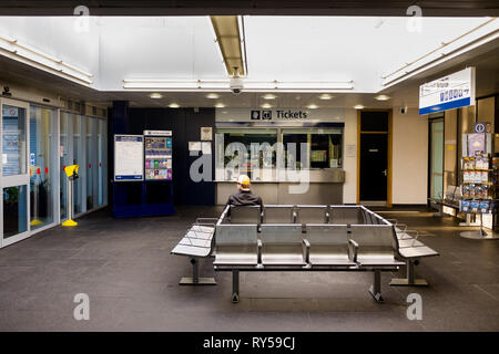 Ein einzelner Mann tragen Baseball Cap von hinten gesehen sitzt allein in den Bahnhof Fort William Wartezimmer. Stockfoto