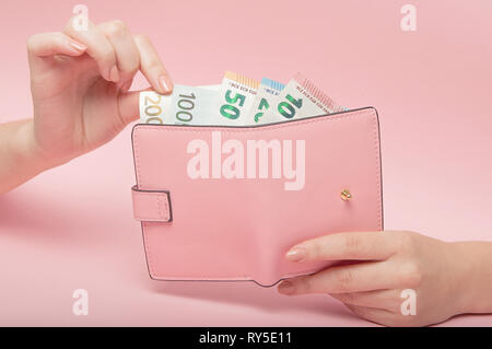 Rosa Geldbeutel und Euro-banknoten in weibliche Hände auf rosa Hintergrund. Geschäftskonzept und Instagram. Stockfoto