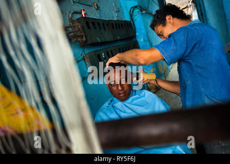 Ein kubanischer Friseur schneidet die Haare eines Menschen in einem improvisierten Friseur in einer Passage des Haus in Havanna, Kuba. Stockfoto