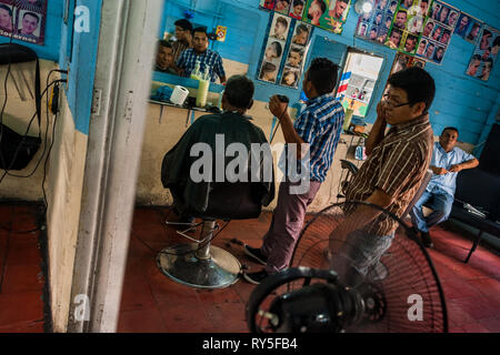 Eine salvadorianische Friseur schneidet die Haare eines Mannes in einem Friseur in San Salvador, El Salvador. Stockfoto