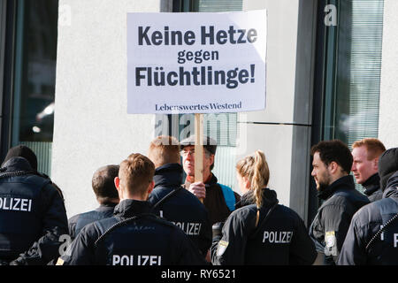 Wiesbaden, Deutschland. 12. März 2019. Einen einzigen Zähler Proteste hält ein Schild mit der Aufschrift "Keine demagogische Propaganda gegen Flüchtlinge außerhalb des Court House. Er ist durch mehrere Polizisten umgeben. Die Gerichtsverfahren gegen die irakische Asylbewerber Ali B. für den Mord an Susanna F. aus Mainz war letztes Jahr in Wiesbaden eröffnet. Mehrere rechtsradikale Organisationen ein Protest außerhalb des Court House gegen Flüchtlinge in Deutschland und für härtere Strafen für Flüchtlinge. Quelle: Michael Debets/Alamy leben Nachrichten Stockfoto