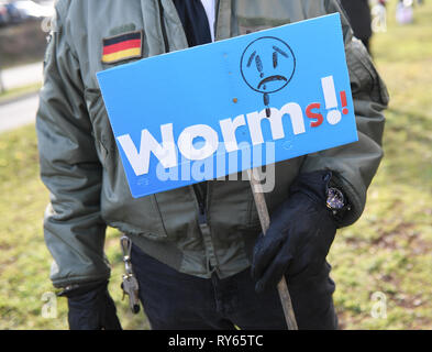 Wiesbaden, Deutschland. 12 Mär, 2019. Ein Mann hält ein Plakat mit der Aufschrift 'Würmer!' vor der Wiesbadener Justice Center während der Vigil. Im Mordfall der 14-jährige Susanna vor dem Bezirksgericht hat begonnen. Der 22-jährige irakische Flüchtlinge Ali B. ist sagte der Schülerin aus Mainz in Wiesbaden im Mai 2018 vergewaltigt und dann getötet schleichend. In Worms, eine junge Frau, die zum Tod in der Nacht des 6. März erstochen worden war, ihre Tunesische ex - Freund ist verdächtig. Credit: Arne Dedert/dpa/Alamy leben Nachrichten Stockfoto