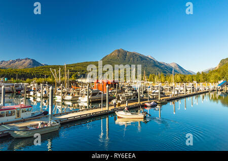 Mann mit Fanggeräten in kleinen Boot Docking am kleinen Hafen Marina Pier entlang der Waterfront auf einem klaren blauen Himmel Tag in den späten Nachmittag. Stockfoto