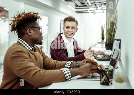 Lächelnd positiver Mann im weißen Hemd aufmerksam zuhören Stockfoto