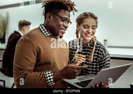 Fröhlicher Kerl mit Dreadlocks tragen Laptop und Informationen erklären Stockfoto