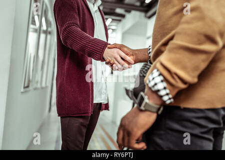 African American Kerl in Gelb pullover Händeschütteln mit hellen Kollegen Stockfoto
