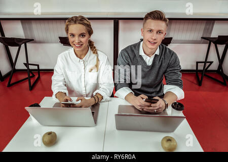 Lächelnd positive Mitarbeiter sitzen Schulter an Schulter, während Sie soziale Medien Stockfoto