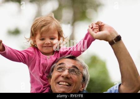 Reifer Mann mit seinem Kleinkind Enkelin eine Schulter reiten. Stockfoto