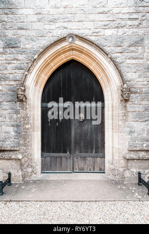 Alte Kirche aus Holz Türen mit schmiedeeiserne Beschläge und Stein gemeißelten Köpfe auf beiden Seiten Stockfoto