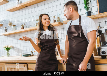 Kassierer in Schürzen sprechen in der Nähe von Bar aus Holz Zähler in Coffee House Stockfoto