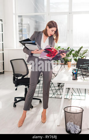 Attraktive Geschäftsfrau, Ordner und lesen Magazin im Amt stehende Stockfoto