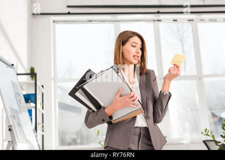 Attraktive Geschäftsfrau, die Ordner und die Zettel mit späteren Beschriftung im Büro Stockfoto