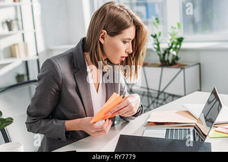 Selektiver Fokus der überrascht Geschäftsfrau holding Paper Plane und Laptop in der Nähe von Einweg- Cup in Büro, procrastination Konzept Stockfoto