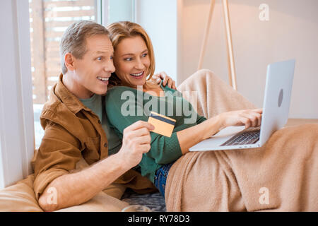 Paar mit Laptop aufgeregt, während Ehemann holding Kreditkarte Stockfoto