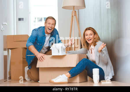 Aufgeregt glückliches Paar angezeigt Haus Modell beim Auspacken Karton Stockfoto