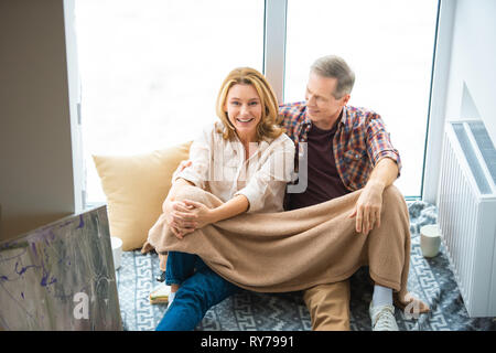 Glückliches Paar sitzen auf dem Boden durch die großen Fenster im neuen Zuhause Stockfoto