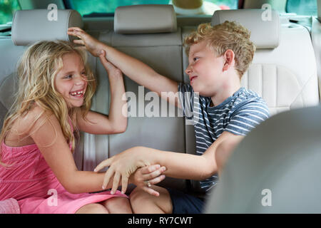 Zwei Kinder kämpfen und streiten miteinander unterwegs im Auto in den Urlaub Stockfoto