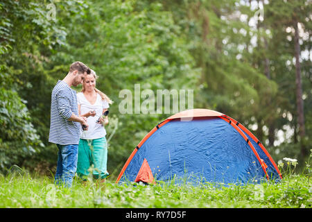 Paar vor dem Zelt beim Camping auf einer Wiese im Sommer Urlaub Stockfoto