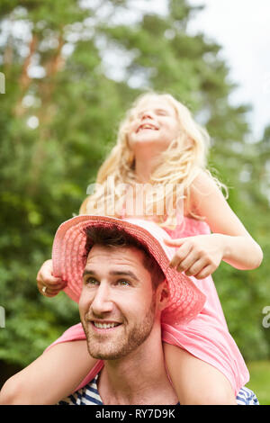 Vater trägt seine fröhliche Tochter huckepack auf den Schultern im Sommer Stockfoto