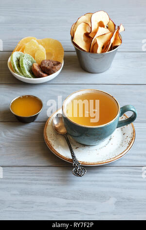 Gesundes Dessert: Stücke von kandierte Ananas, Ingwer, getrocknete Feigen, Apple Chips und Honig in kleinen Schüsseln und eine Tasse grünen Tee auf einem grauen Holz- ta Stockfoto