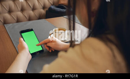 Junges Mädchen hält Smartphone mit Green Screen in Cafe Stockfoto