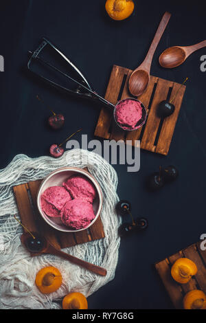 Hausgemachte rosa Eis in Eis Löffel mit Kirschen und Pflaumen. Dunkle essen Fotografie mit Kopie Raum Stockfoto