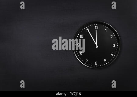 Schwarze Uhr mit fünf Minuten vor Mitternacht am Schwarzen Schiefertafel Hintergrund. Office clock angezeigt, 5 min. bis 24.00 oder 12.00 Uhr Stockfoto