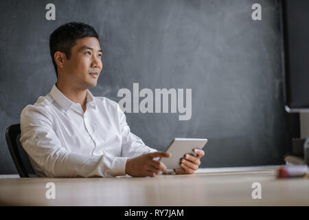 Asiatische Geschäftsmann denken während der Arbeit auf einem Tablet Stockfoto