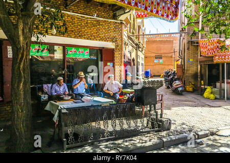 Kashgar Altstadt uigurischen Männern Vorbereitung Lamm am Spieß Straße Essen und Tee trinken. Stockfoto