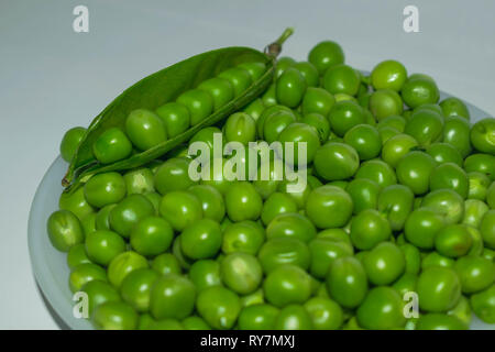 Green pea pod, grüne Erbsen in einer weißen Schüssel auf einem weißen Hintergrund. Stockfoto