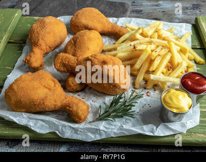 Knusprig gebratene Hähnchenschenkel panierte goldene Farbe, Pommes Frites, Sauce, Holz- Hintergrund Stockfoto